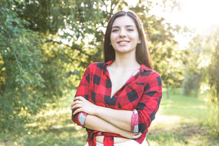 Smiling beautiful brunette girl in a red, plaid shirt, with arms crossedの写真素材