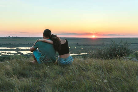 Couple is hugging and sitting close on a hill at sunsetの写真素材
