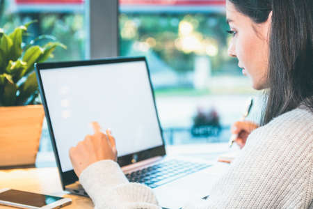 Closeup of a woman working on laptop with white screen, holding a penの写真素材