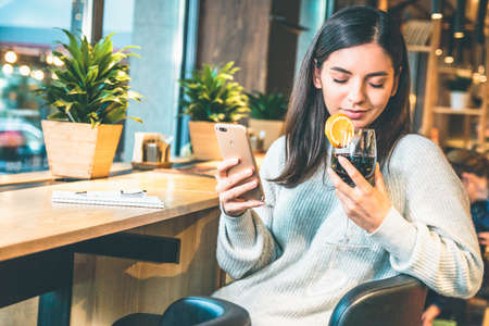 Christmas concept - Happy young woman with glass of wine or glintwine checking the phoneの写真素材