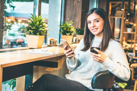 Christmas concept - Happy young woman with glass of wine or glintwine checking the phoneの写真素材