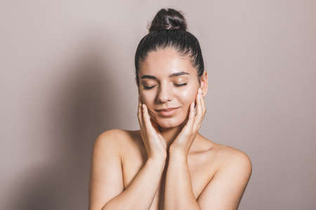 Beautiful woman with clean natural skin and eyes closed touching her faceの写真素材