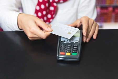 Hands of a female shop assistant holding a credit card and making payment wireless.