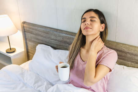 woman sitting on bed with eyes closed holding a cup of coffee or teaの写真素材