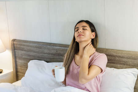 Woman sitting on bed drinking coffee smilingの写真素材