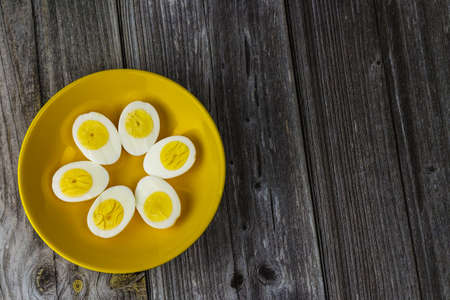 Boiled egg halves in a yellow bowl on wooden table.の写真素材