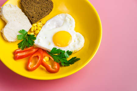 heart-shaped fried egg and bread in a yellow plate on a red background. valentines day concept.の写真素材