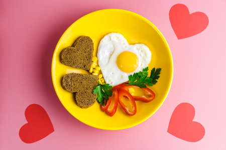 valentine's day breakfast. heart-shaped fried egg and bread in a yellow plate on a red background.の写真素材