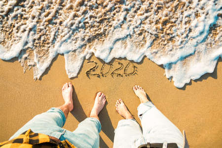 Top view legs of a couple on sandy beach and year 2020 on it, wave approaching.の写真素材