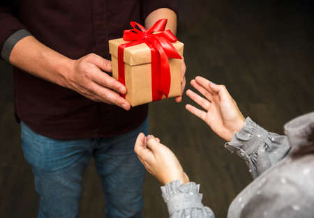 Close up view of hands of a man handing a gift package with a bow to a woman.の写真素材