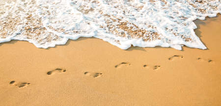 footprints on a clear sandy beach and a clean white wave.