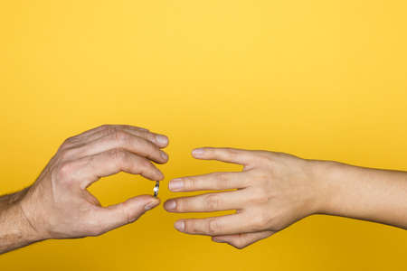 close up of man hand putting an engagement ring on a woman hand on yellow background.の写真素材