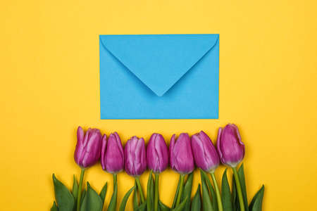 Pink, purple tulips and blue coral envelope with one red heart on it on yellow backgroundの写真素材