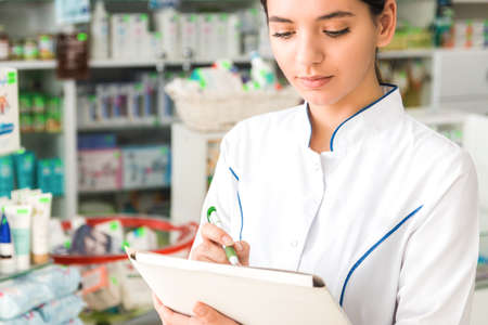 close up pharmacist with neutral emotions on face making notes in storeの写真素材