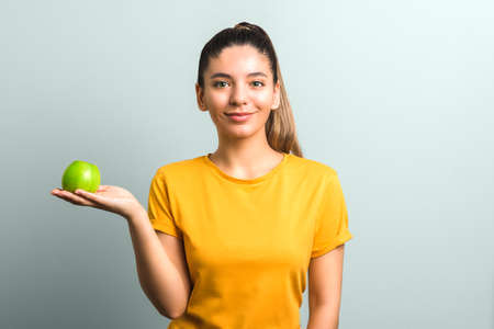 beautiful girl in yellow t-shirt holding green apple in palm with copy space. idea designの写真素材