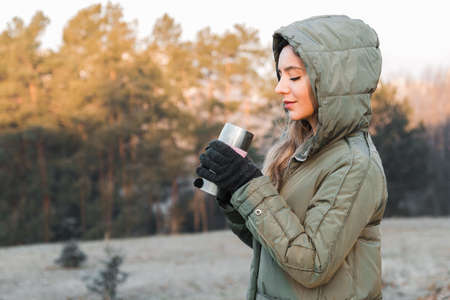 cold in the mountains. woman tourist outdoor at sunrise holding a flask with tea or coffee and getting warmの写真素材
