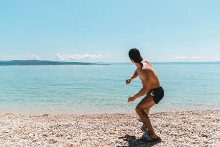 young man traveler with hat on at seaside throwing stones into the ocean. time to relax.の写真素材
