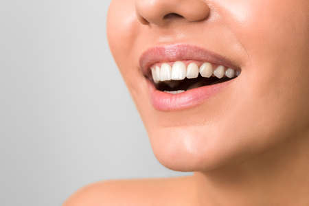 wide and beautiful smile of a young woman with clean skin and white teeths against grey background