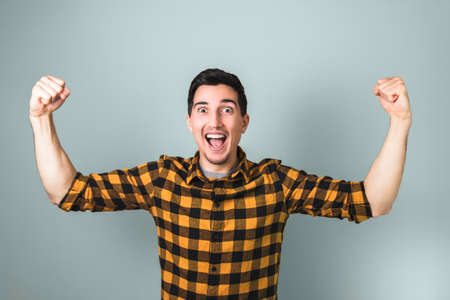 winner in life. happily excited handsome man with nice smile in yellow shirt with both arms raised up on grey background.の写真素材