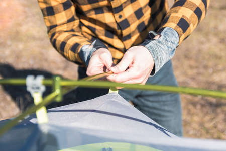 close up view man in yellow shirt sets up tent in mountains in springtime