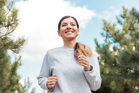 healthy lifestyle. cheerful attractive woman running in park with pine trees in the morningの写真素材