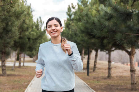 healthy lifestyle. cheerful attractive woman running in park with pine trees in the morningの写真素材