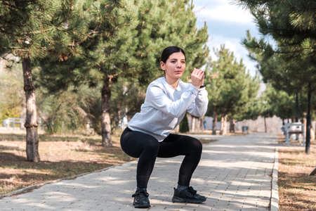 healthy lifestyle. cheerful attractive woman doing exercises and stretches in a park with pine trees in the morningの写真素材
