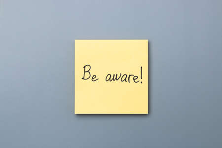 be aware on yellow sticky note over a grey background. april fools day.