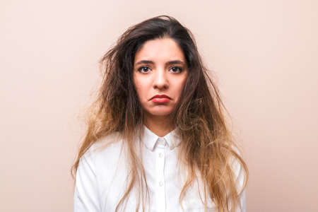 sad woman with tangled hairs in white shirt against pink background. morning womans routine