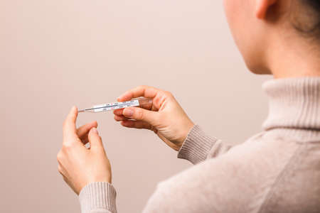 closeup woman hands holding a glass thermometer with high temperature above thirty eight....