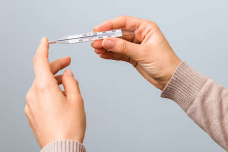 closeup woman hands holding a glass thermometer with high temperature above thirty eight. coronavirus symptoms.の写真素材