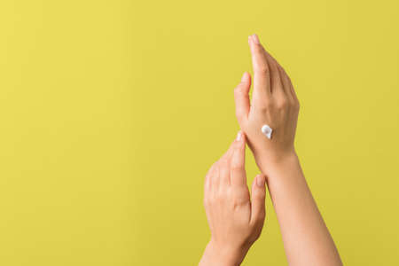 closeup of tender hands of a young woman with moisturizer on against yellow background. spring skin...