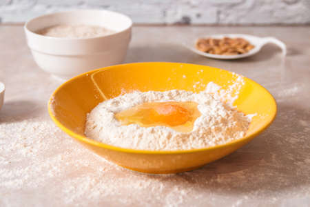 baking ingredients, flour, salt, eggs and oil in white and yellow bowls on marble countertop in...