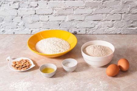 baking ingredients, flour, salt, eggs and oil in white and yellow bowls on marble countertop in bright homey kitchen.の写真素材