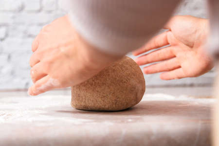 process of baking health bread at home. low angle closeup woman hands kneading dough from rye flour on marble countertop in bright kitchen.の写真素材