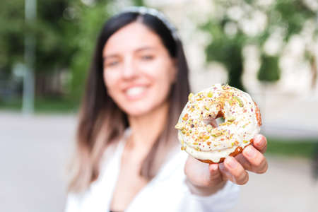 closeup of delicious and colorful donut in hand of a woman defocused in city park. junk sweet and tasty fast food dessert .の写真素材