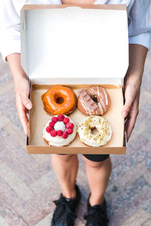 close up hands holding four pieces of totally different colorful and delicious looking donuts in...