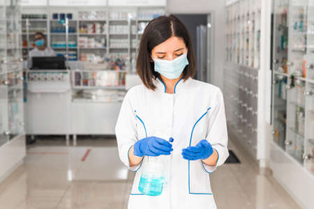 turkish woman doctor or pharmacist with medical mask on face using disinfectant in pharmacyの写真素材
