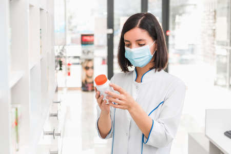 choosing the right medicine. professional looking female pharmacist with medical mask on in drug...