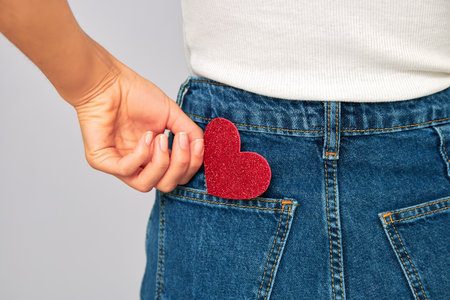 woman holding a small sparkling red heart putting it in or taking off the pocket of her jeans. Sharing and receiving Valentines, keeping love on youの写真素材