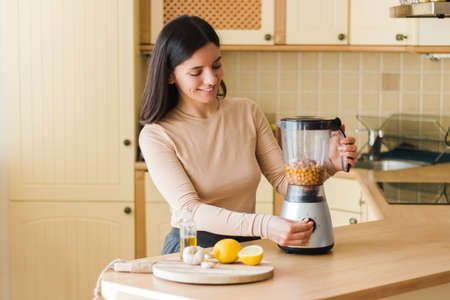 Beautiful ethnicity woman 25-30s with attractive smile in the kitchen preparing natural vegetarian food. homemade chickpeas hummus recipeの写真素材