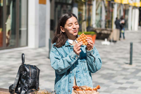 attractive girl eating with big pleasure tasty food from take away cafe in the street. you deserve itの写真素材