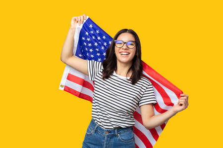 young cheerful multi ethnicity female holding american flag against yellow backgroundの写真素材