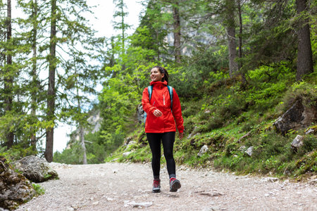 Fearless young woman hiking cheerfully alone in the mountain forest in a red raincoat looking towards the sideの写真素材