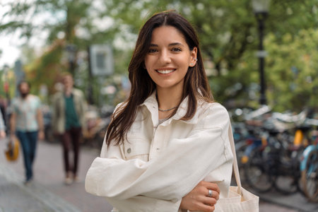 Portrait of multiethnic strong LGBT gorgeous woman confidently smiling hugging herself on the street of blurred city in backgroundの写真素材