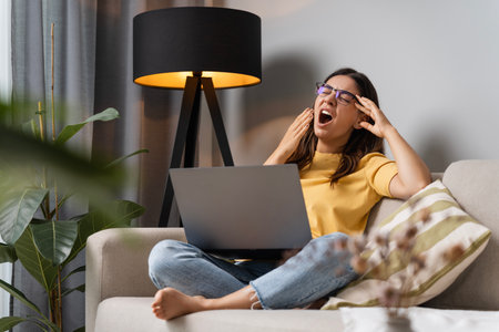 Overworking multi-ethnic attractive woman yawning tired student working on laptop in the evening at homeの写真素材