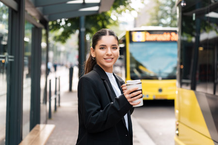 Beautiful young multiracial hispanic business woman using public transportation in city smiling and holding eco thermo cup with coffeeの写真素材