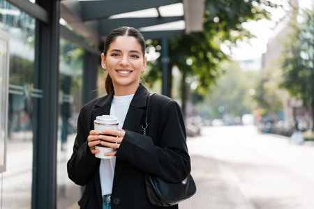 Beautiful young multiracial hispanic business woman using public transportation in city smiling and holding eco thermo cup with coffeeの写真素材