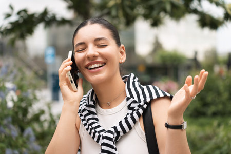 A young professional, phone in hand, walks through an urban park with a confident smile. Dressed stylishly, she balances her roles as a student and businesswoman, symbolizing modern career successの写真素材
