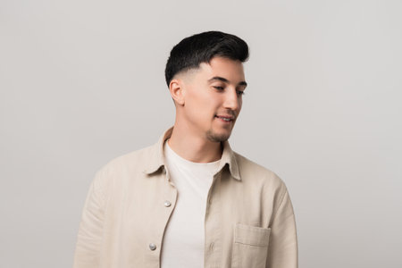 Earphones mockup blending fashion and tech. Stylish man in a beige overshirt gazing downward with a thoughtful expression, captured in a modern studio settingの写真素材